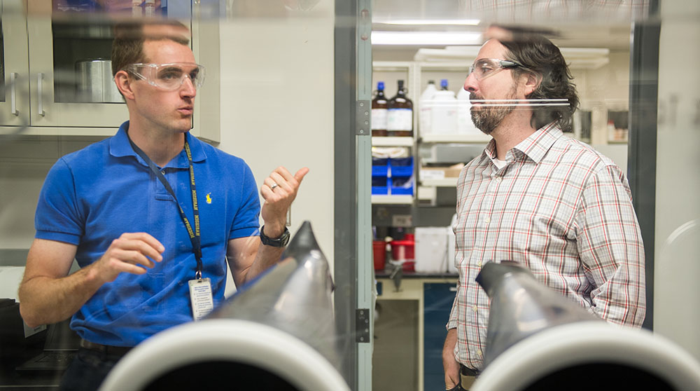 Two scientists wearing safety glasses collaborate in a lab.